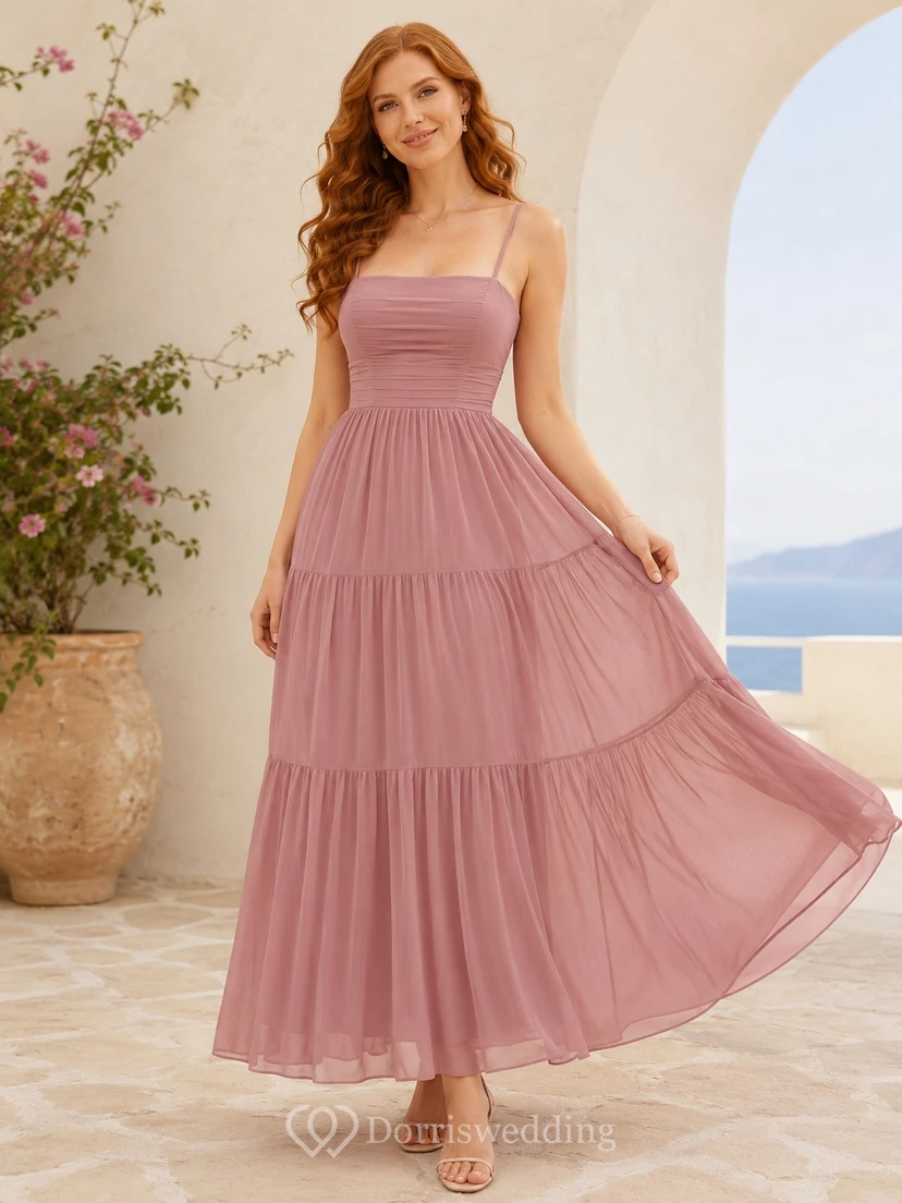 Robe fluide à bretelles spaghetti, sans manches, en mousseline rose poudré, longueur thé, à volants et coupe trapèze, sans manches.