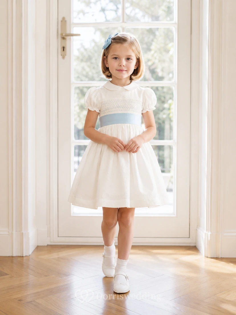 Vestido de niña de flores de satén color marfil con corte en A, mangas cortas abullonadas, escote joya y falda hasta la rodilla con detalles de lazos.