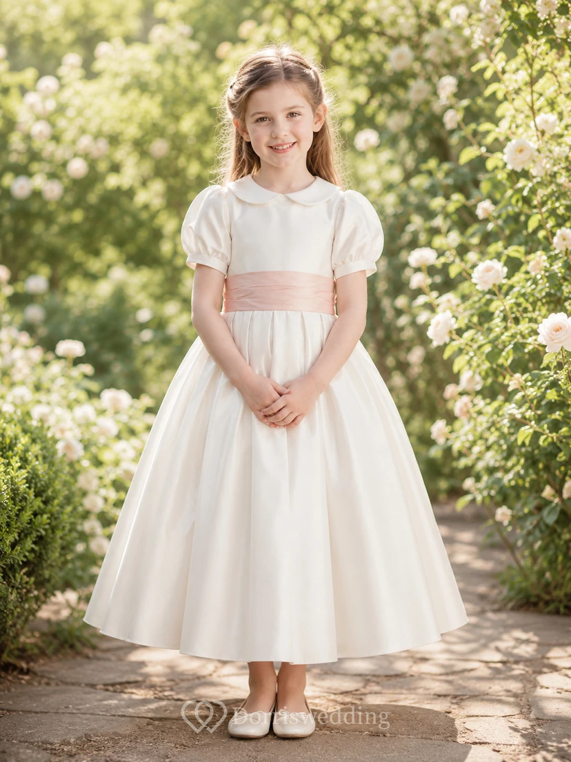 Vestido de niña de flores de satén color marfil con corte en A, mangas cortas abullonadas, escote joya y falda a la altura de la rodilla con detalles de lazos.