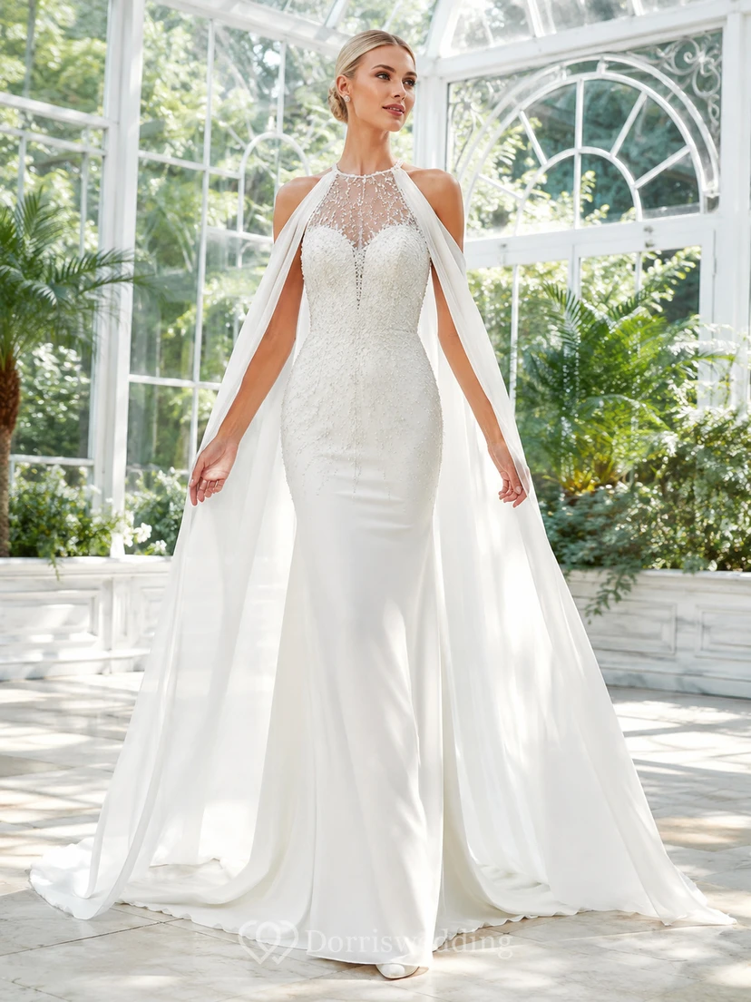 Robe de mariée fourreau en satin et mousseline de soie, col montant illusion, manches cape et traîne amovible, idéale pour une destination.