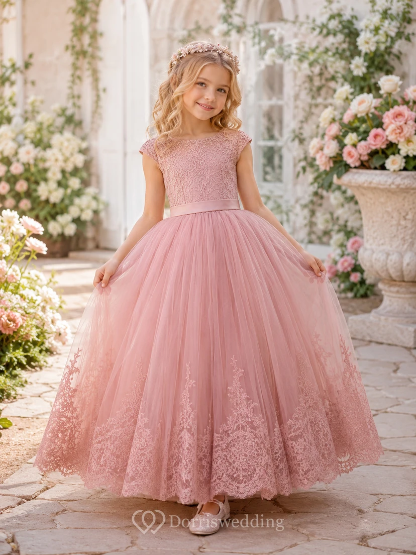 Robe de demoiselle d'honneur en tulle et dentelle rose poudré, coupe trapèze, sans manches, ornée d'appliqués floraux et d'un nœud.