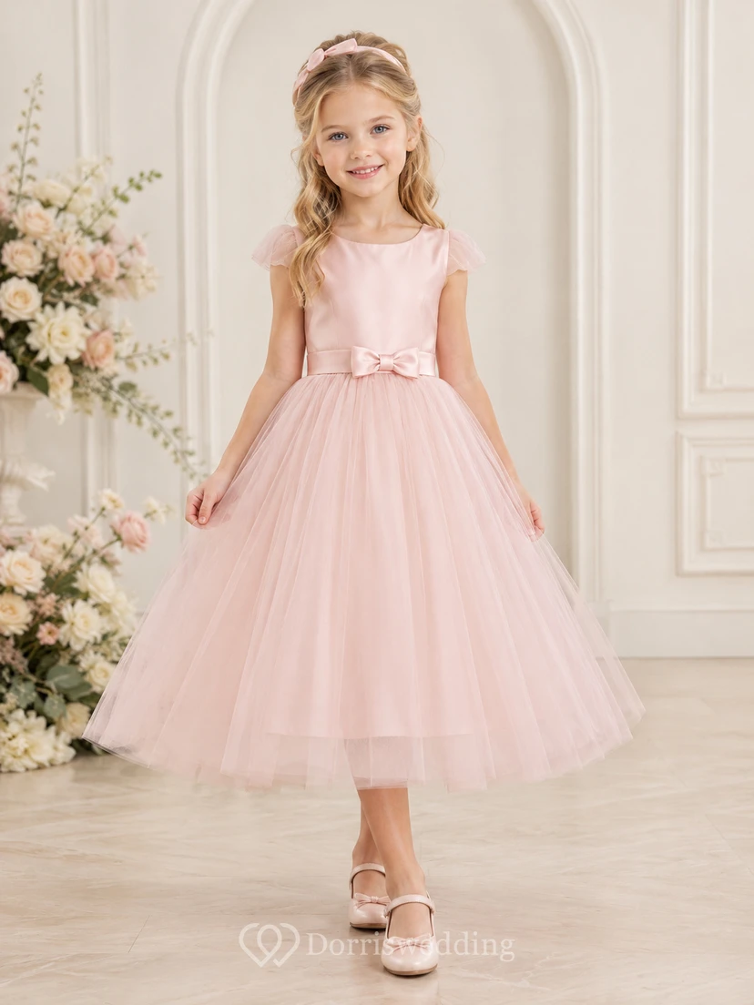 Robe de demoiselle d'honneur en tulle rose poudré, coupe trapèze, manches à volants, longueur thé, avec nœud. Idéale pour un mariage champêtre.
