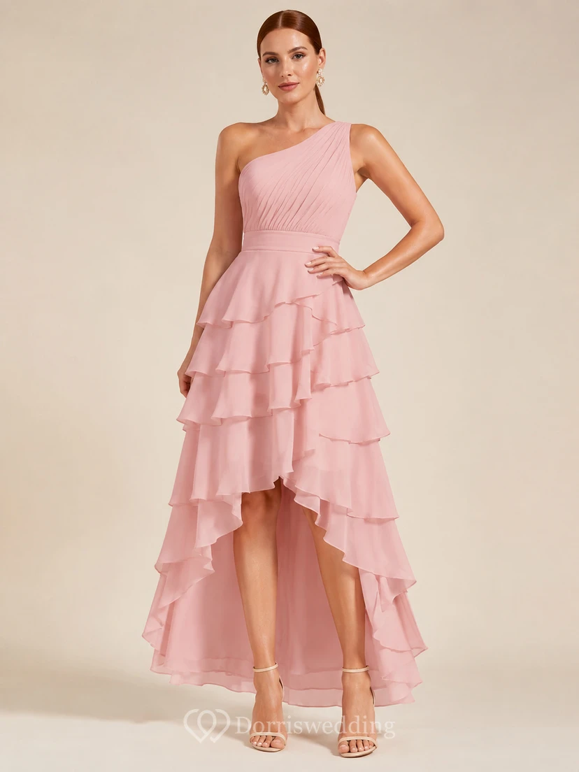 Robe trapèze en tulle rose poudré à une épaule, à volants et ourlet asymétrique.