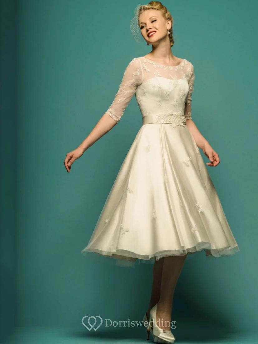 Vestido de novia de corte A, largo hasta la rodilla, con mangas ilusión, escote redondo y apliques de tul.