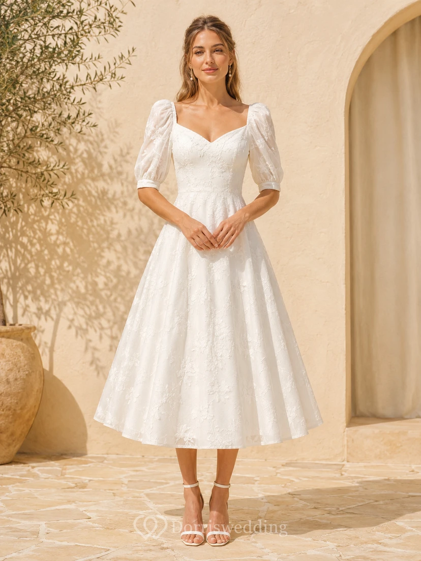 Robe de mariée mi-longue en dentelle, décolleté cœur, manches bouffantes, fermeture éclair au dos nu.