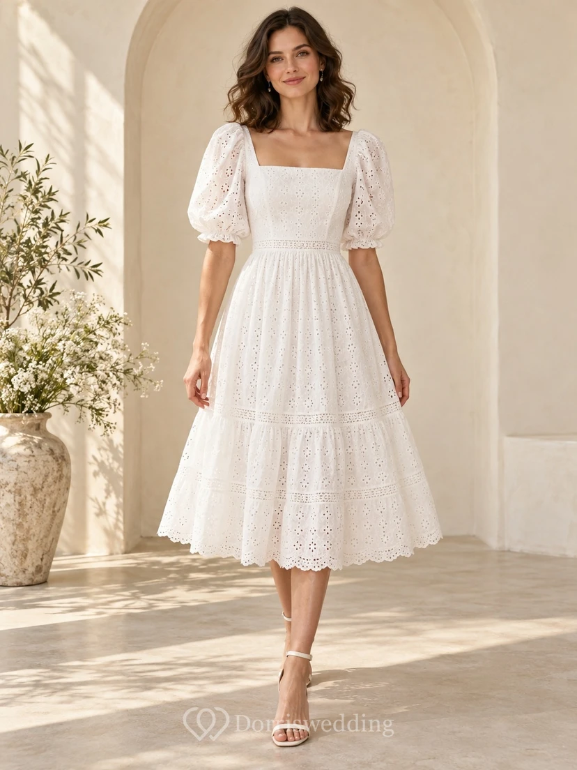 Vestido de novia romántico de corte A, largo hasta la rodilla, escote cuadrado, mangas abullonadas, volantes con ojales y detalles festoneados.