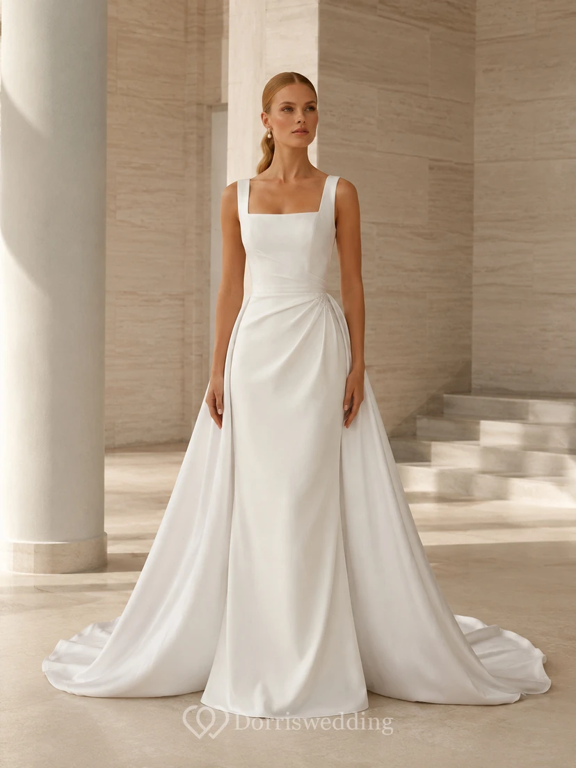 Robe de mariée style domaine, en satin transparent, bretelles carrées, sans manches, coupe trapèze, traîne courte et surjupe drapée.