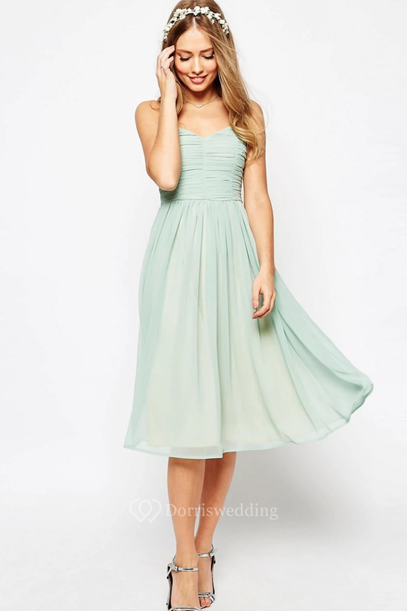 Vestido de dama de honor de gasa verde salvia, largo hasta la rodilla, corte en A, fruncido, sin mangas y con tirantes finos.