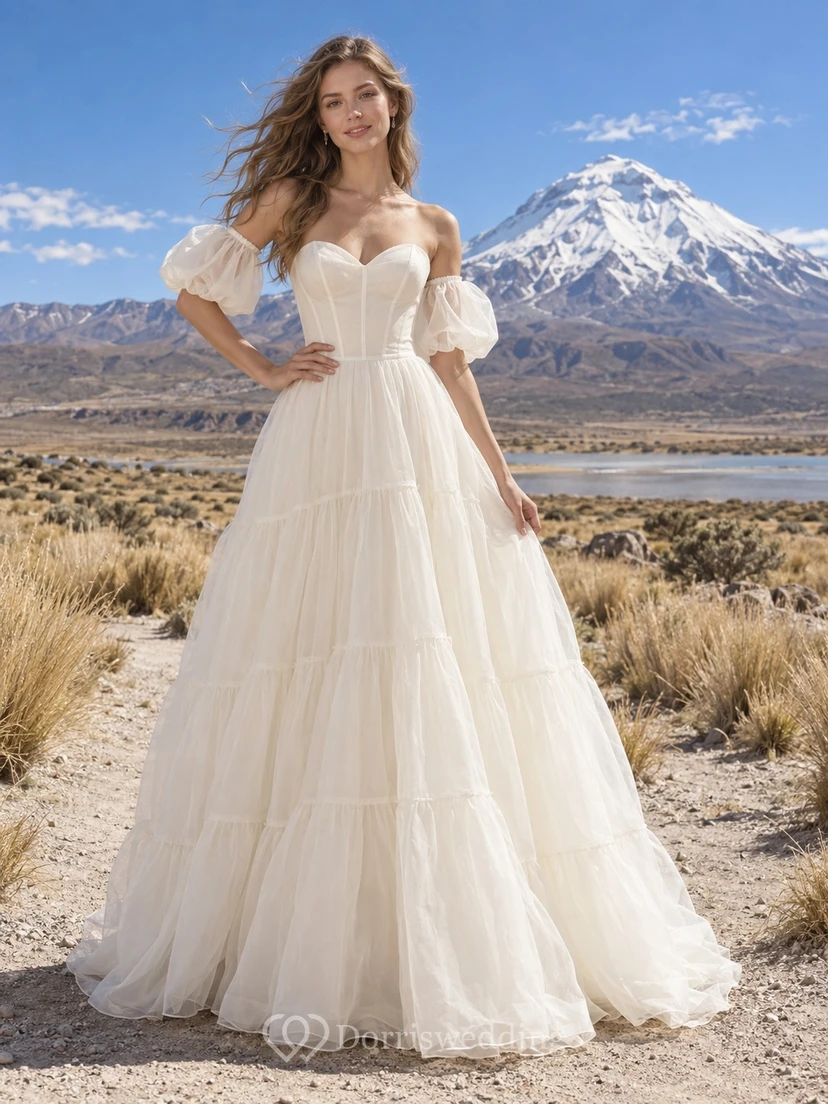 Vestido de novia bohemio de organza con corte en A, escote corazón, mangas abullonadas y falda escalonada.
