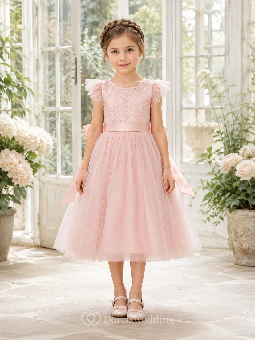 Robe de demoiselle d'honneur en tulle rose poudré à manches à volants, coupe trapèze, avec nœud, en dentelle et longueur thé. Idéale pour un mariage champêtre.