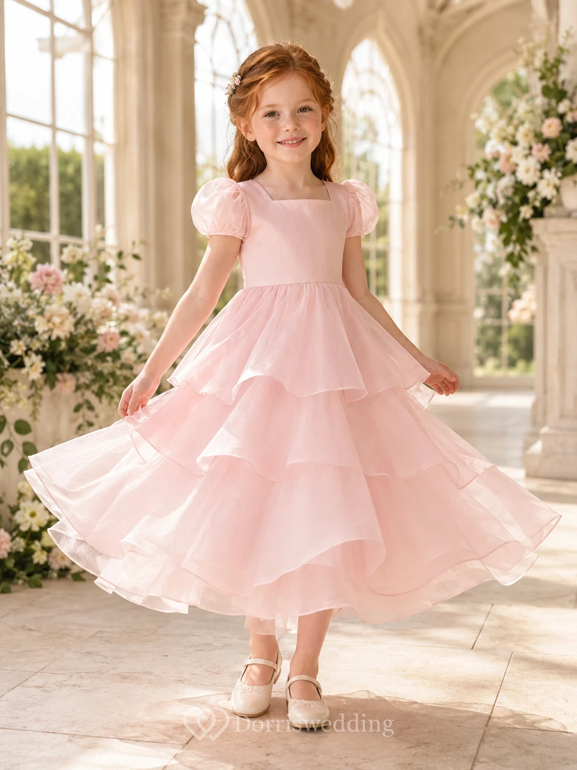 Robe de demoiselle d'honneur en organza rose poudré, coupe trapèze, manches courtes, col rond, jupe mi-longue, détails à volants