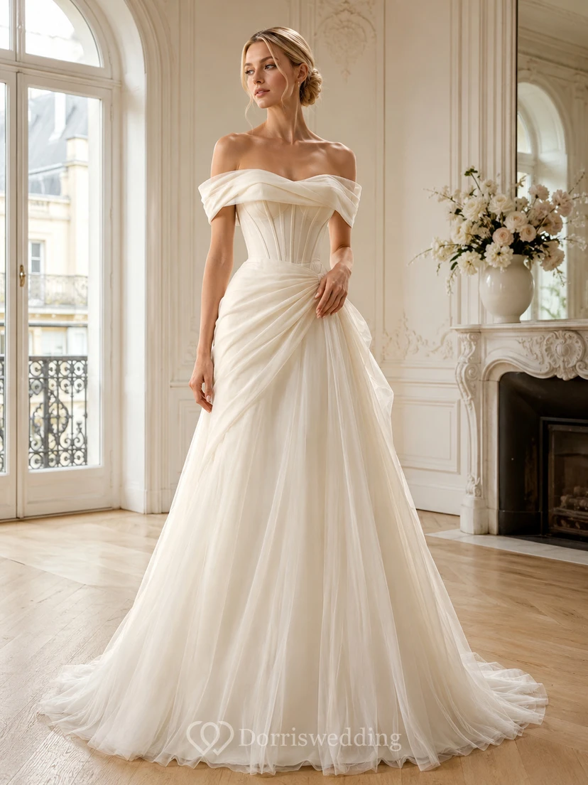 Robe de mariée architecturale en tulle, épaules dénudées, manches courtes, coupe trapèze, traîne et fronces, style jardin.