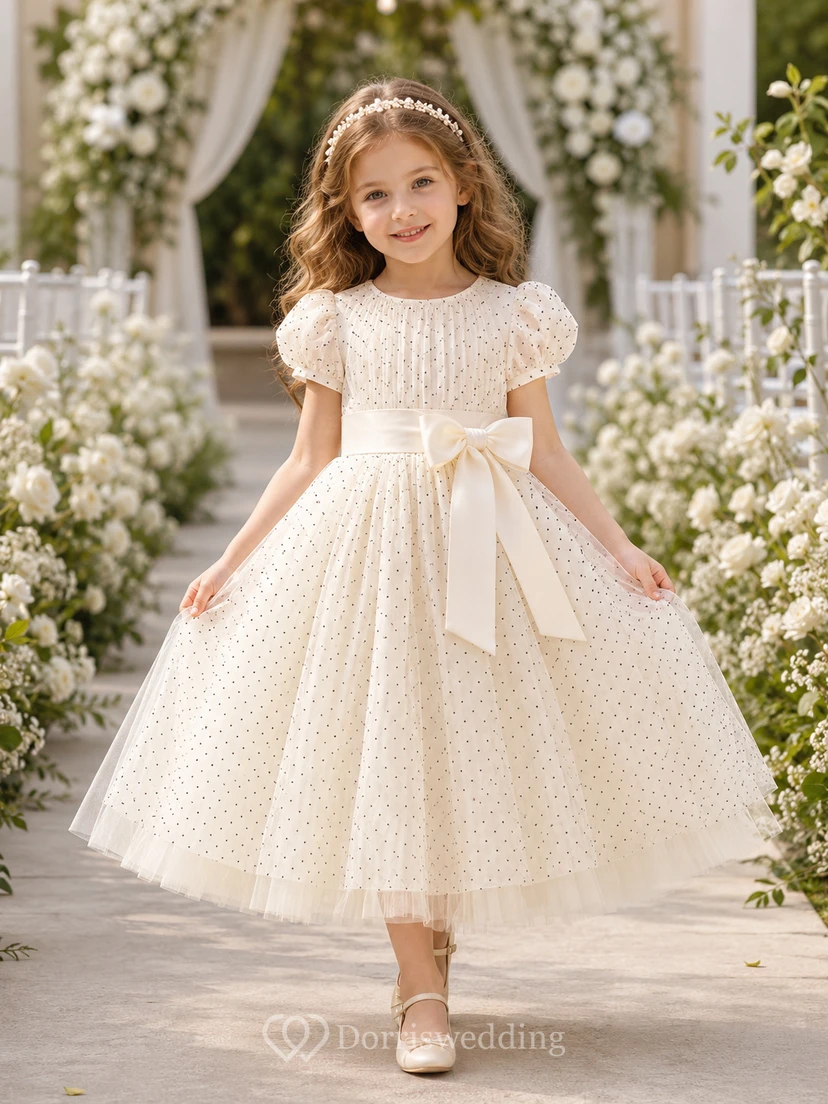 Vestido de niña de flores de tul color marfil con lunares, corte en A, manga corta, cuello redondo, fajín con lazo, largo hasta la rodilla.